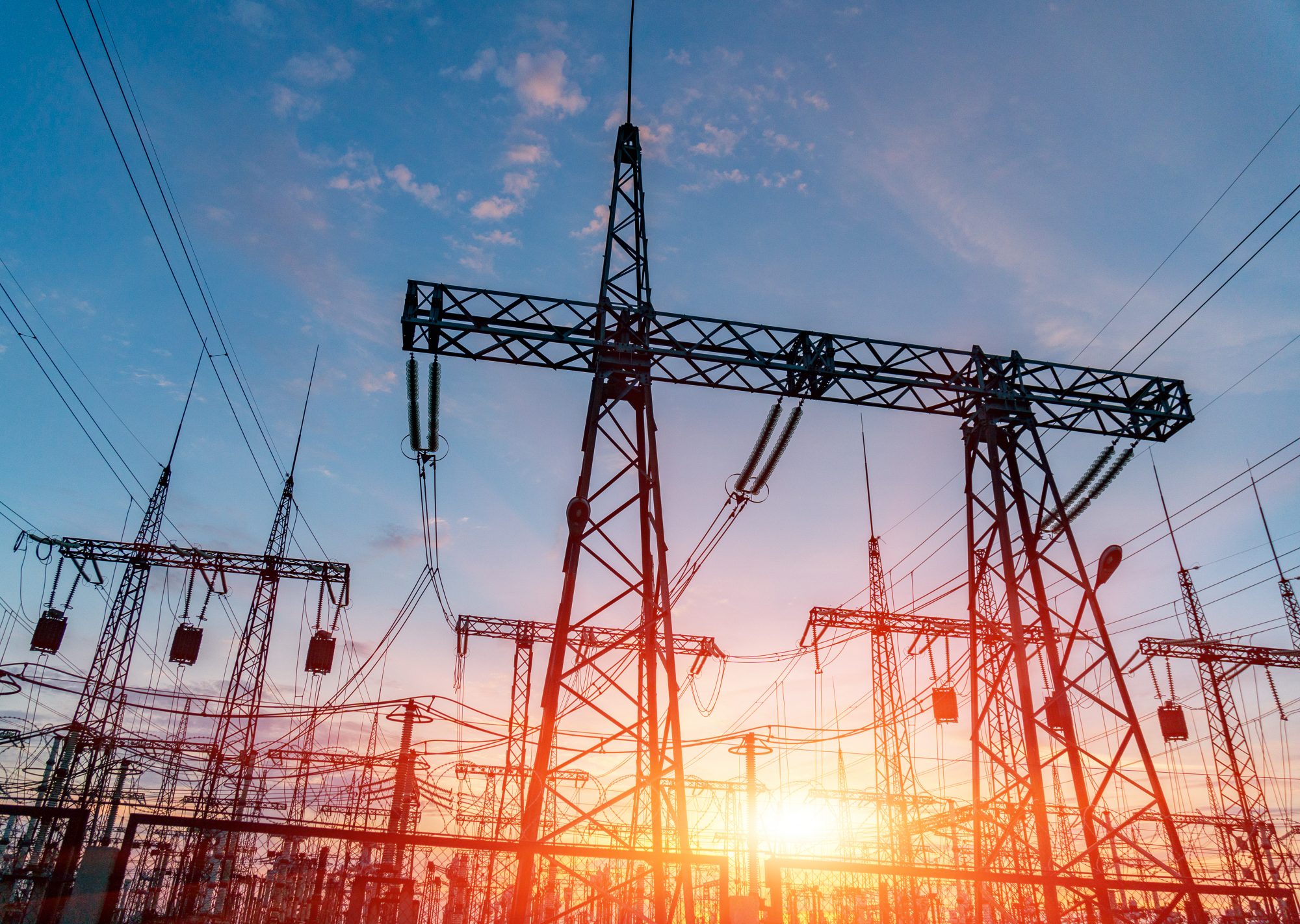 High-voltage power lines and transformers at an electricity distribution station at sunset.