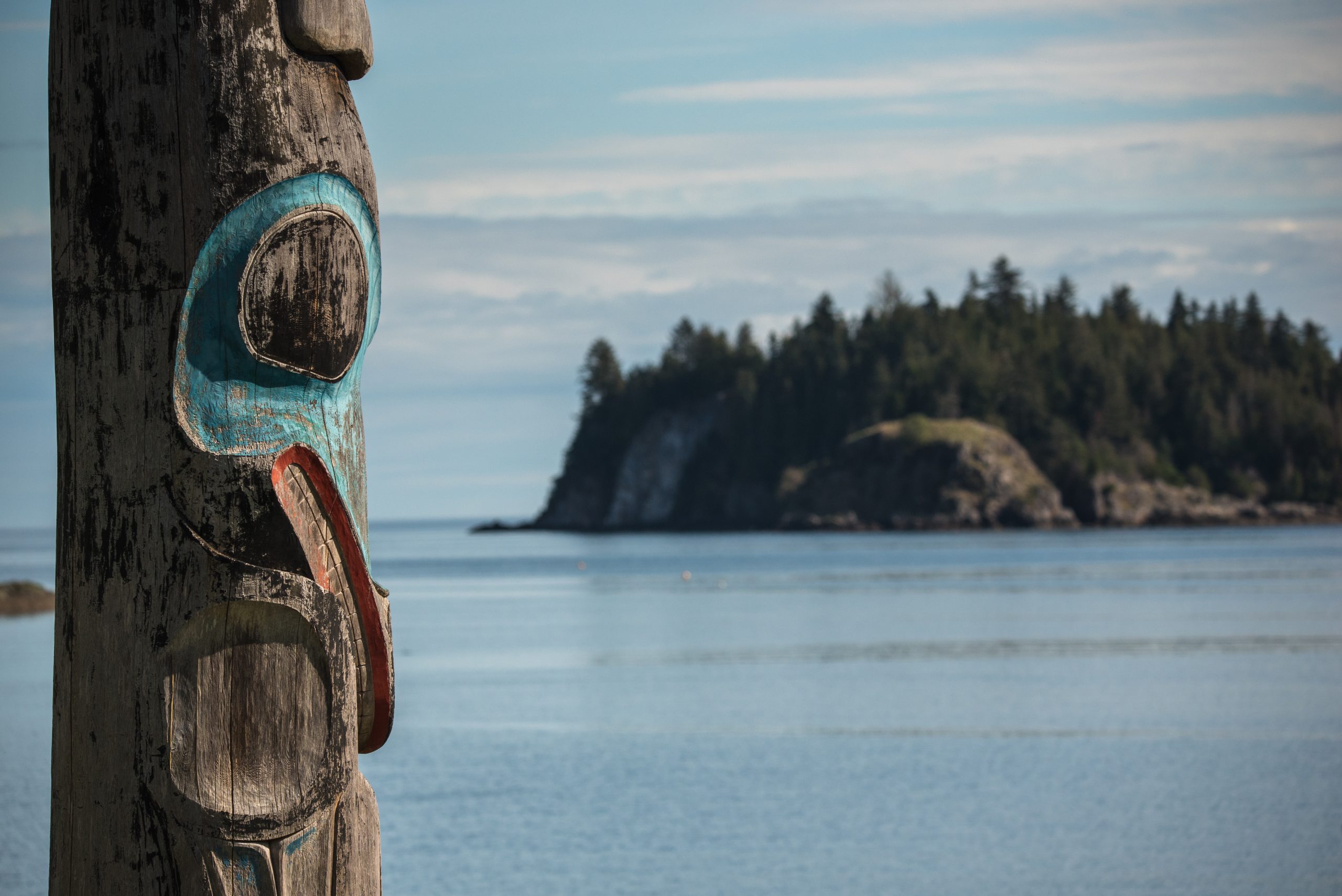 a close up of a Totem pole with a view of the ocean in the background.